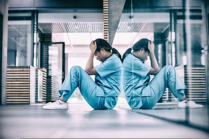Stressed,Nurse,Sitting,In,Hospital,Corridor